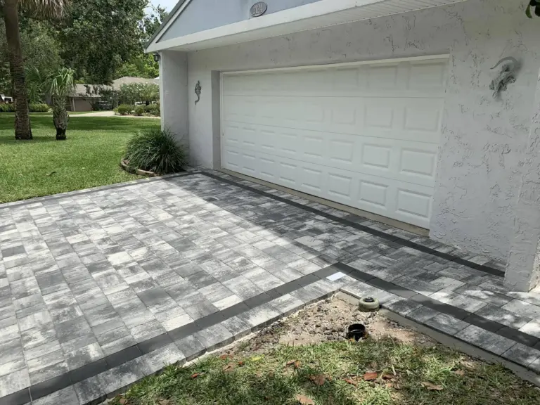 Gray and white driveway pavers framed by a dark border beside a white garage.