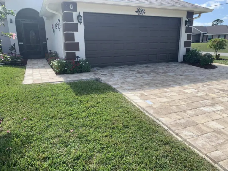 Tan driveway pavers joining a matching walkway toward a home’s front entrance.