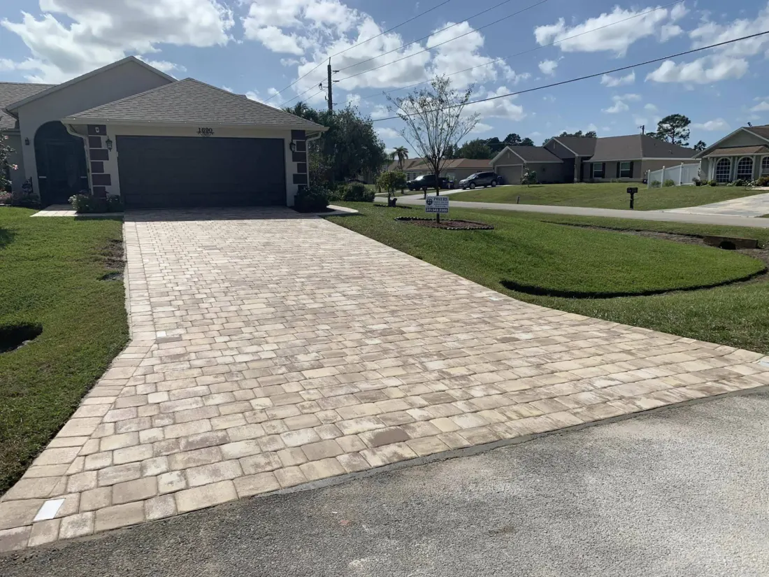 Tan driveway pavers with a widened entrance leading to a home’s dark garage.