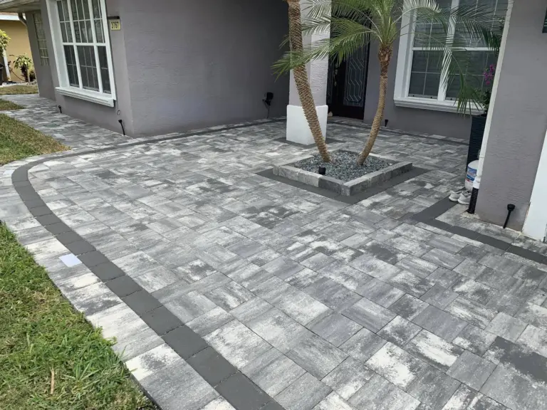 Gray and white entrance pavers with dark borders around a palm planter and porch columns.