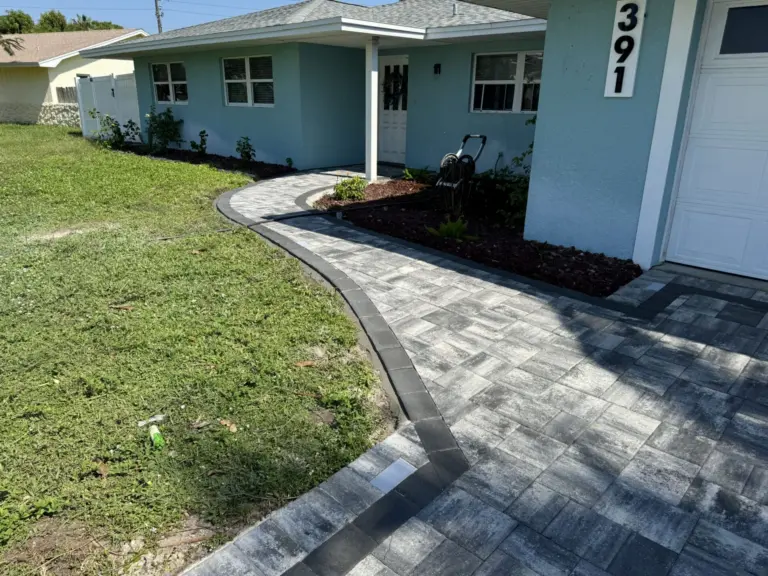 Curved gray paver path beside lawn and a planted bed outside a blue home.