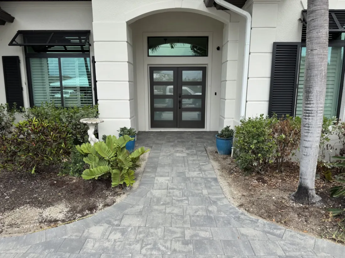 Gray front entrance pavers leading between planting beds to dark double doors.