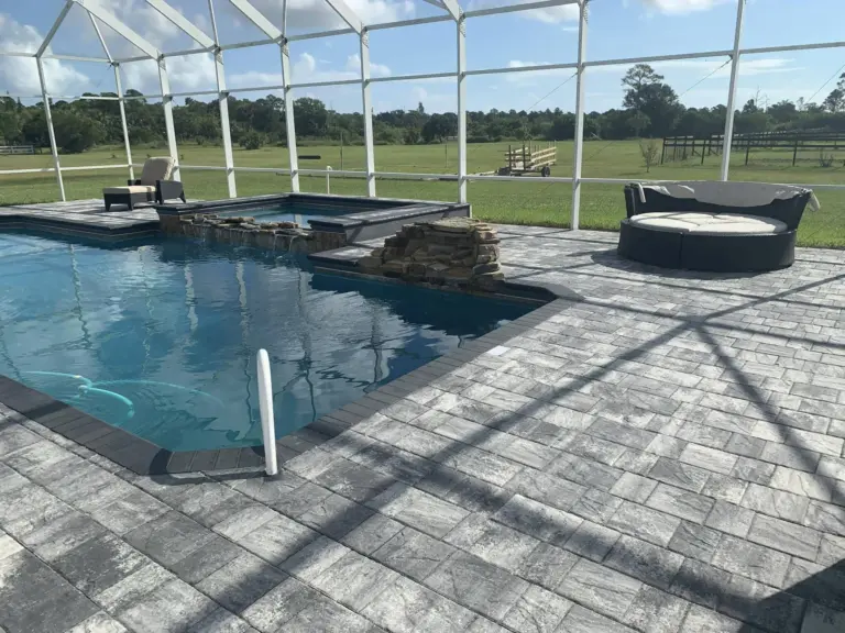 Gray patterned pool deck pavers connecting a screened pool, raised spa, and covered patio.