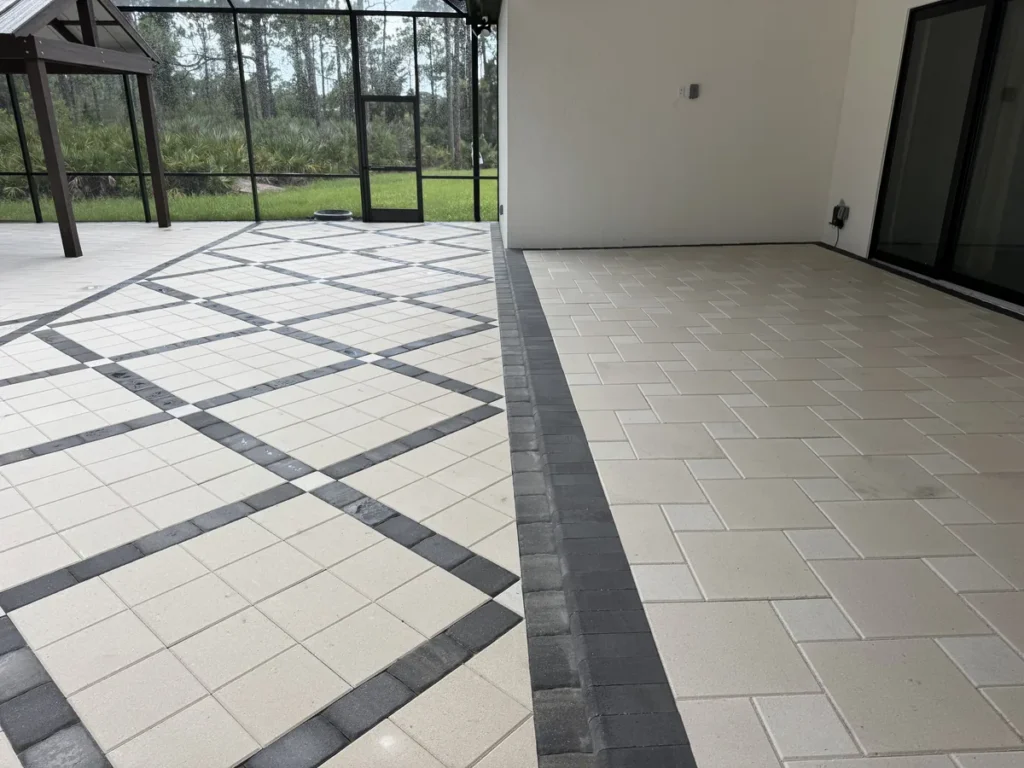 Charcoal border separating a raised cream paver patio from the patterned paving below