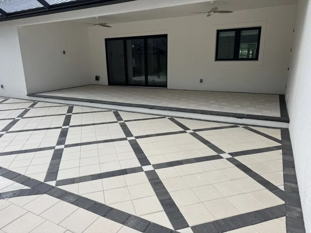 Cream paver patio with charcoal diamond bands beside a raised covered patio